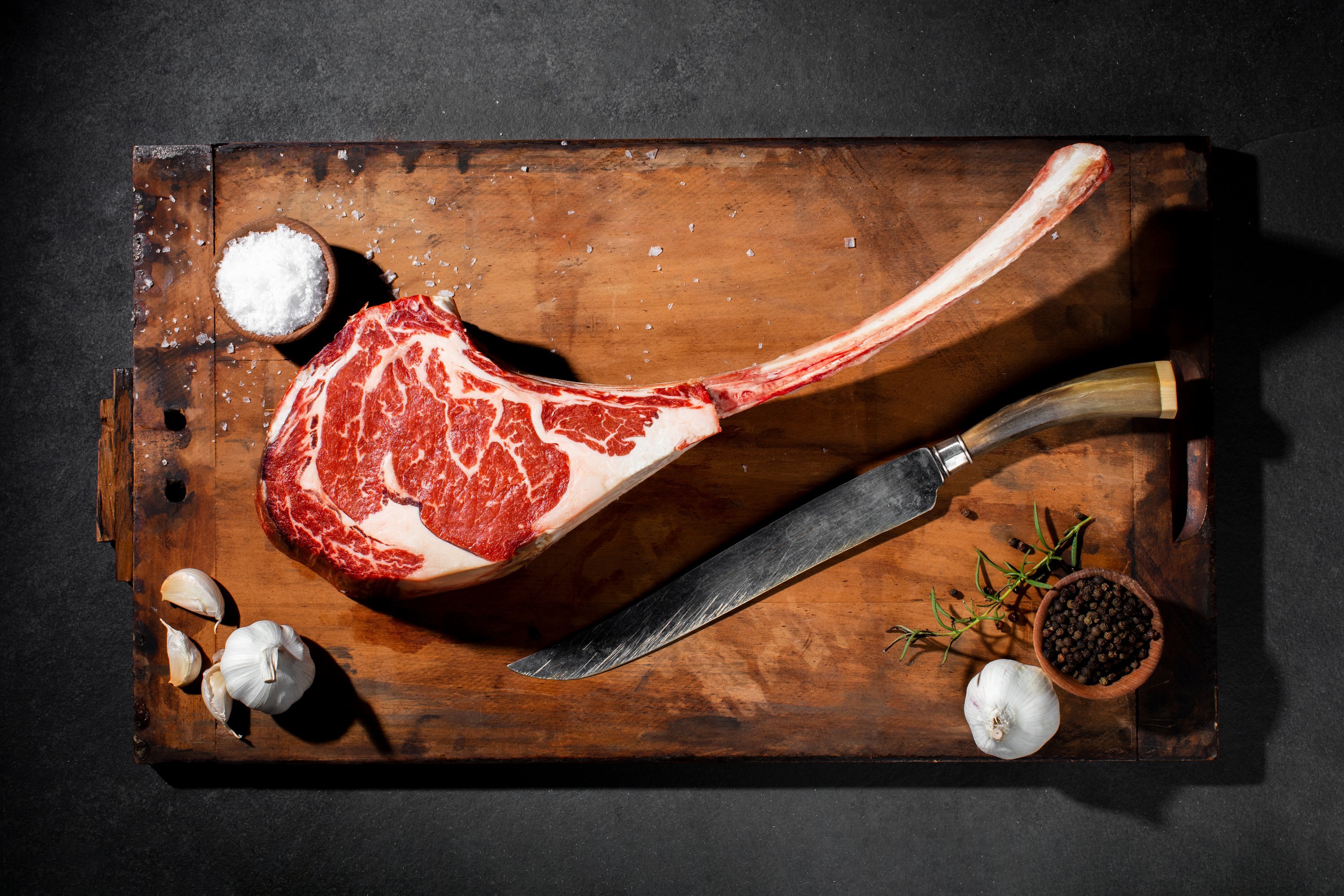 A thick, raw tomahawk steak with a long frenched bone and rich marbling rests on a rustic wooden cutting board.