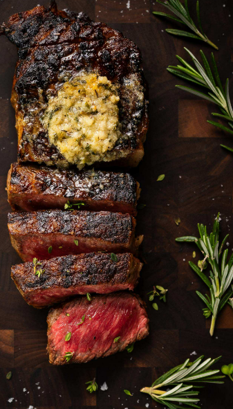 11 Incredible Compound Butter Recipes for Steak A close-up view shows a cooked, sliced steak with butter melting on top and surrounded by rosemary.
