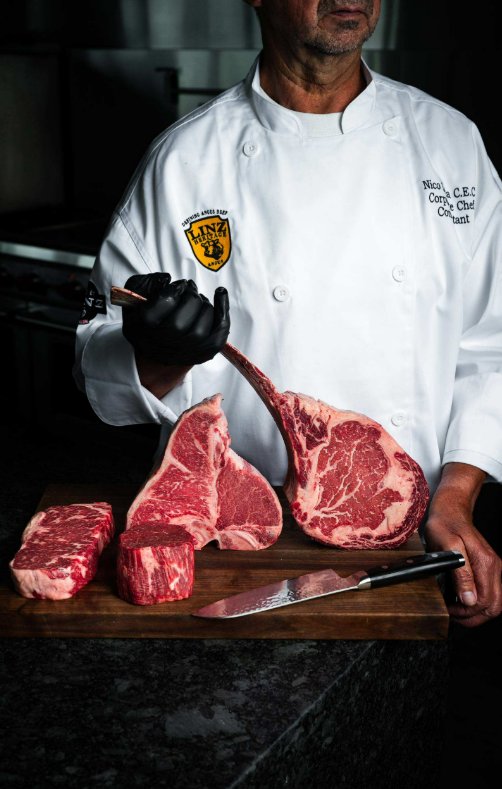 Why Sourcing 100% Black Angus Beef Makes a Difference in Premium Steaks A man wearing a white chef's jacket is holding the bone of a steak while wearing a black glove.